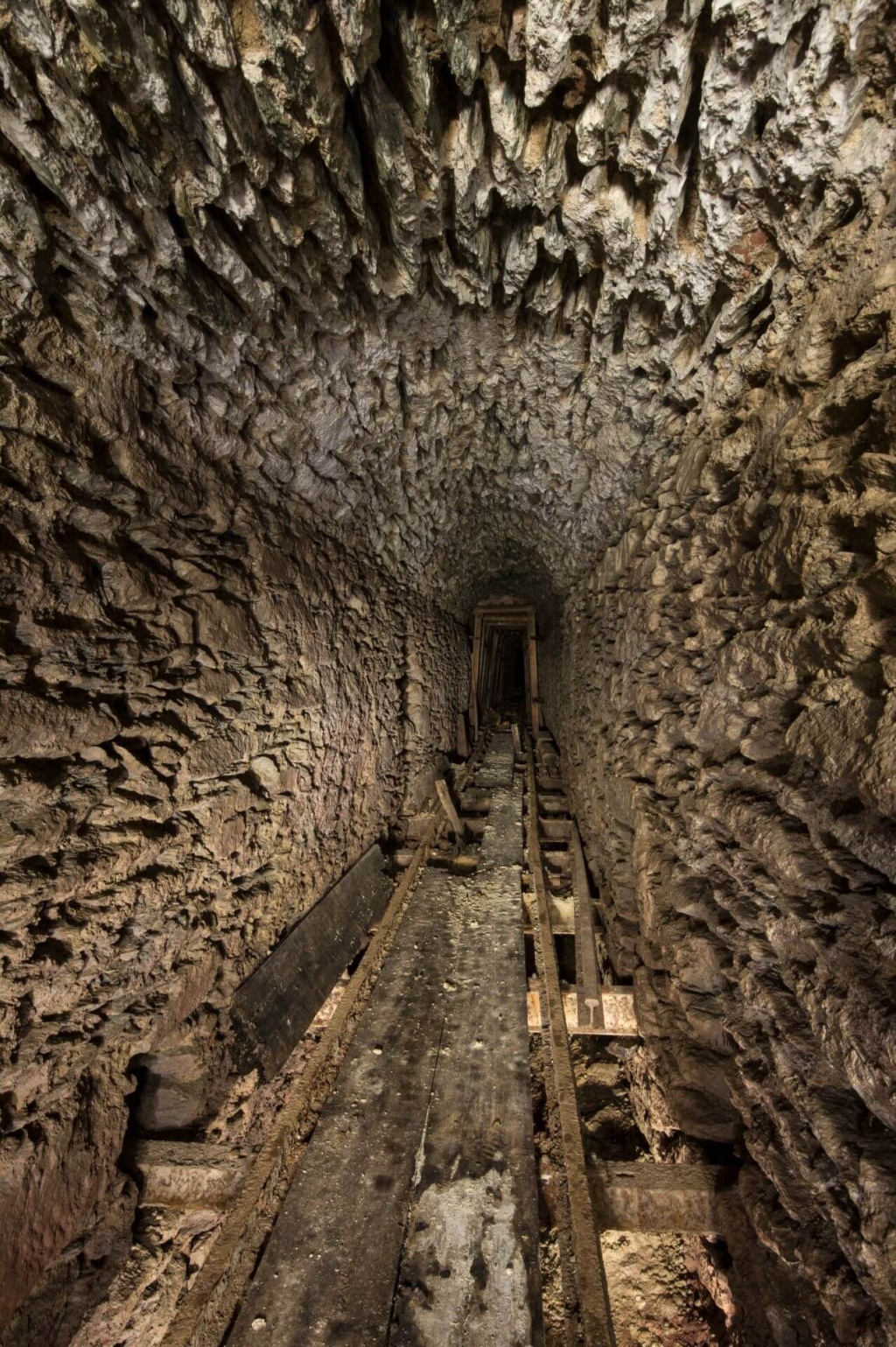 Zeigt den schroffen Ausbau des Wasserlösestollens, mit Gleisen in der Mitte und Bretter zum Laufen.