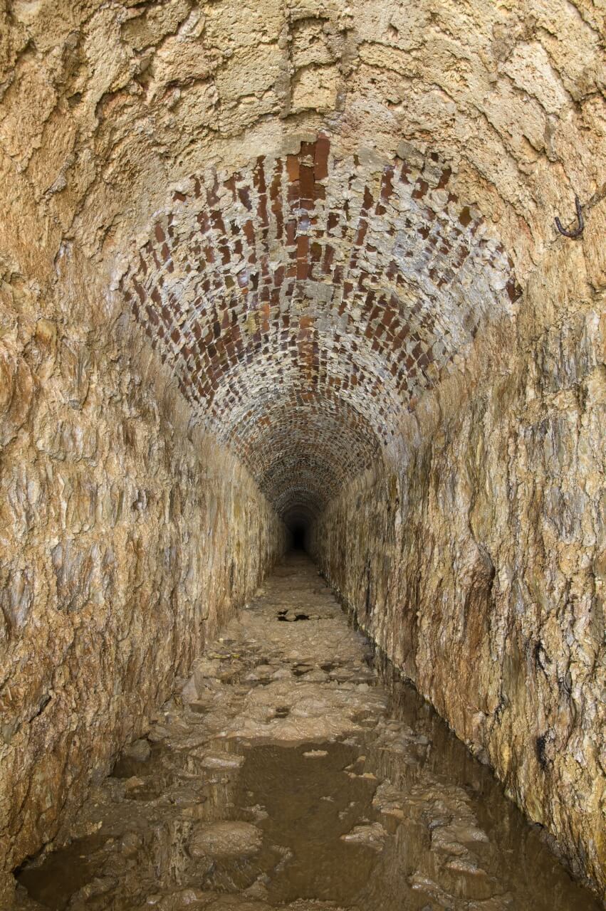 002-tortenstollen Zeigt den absolut geradlinigen Hauptstollen mit seinem Ausbau aus Naturstein und Gewölbedecke aus Ziegelstein.