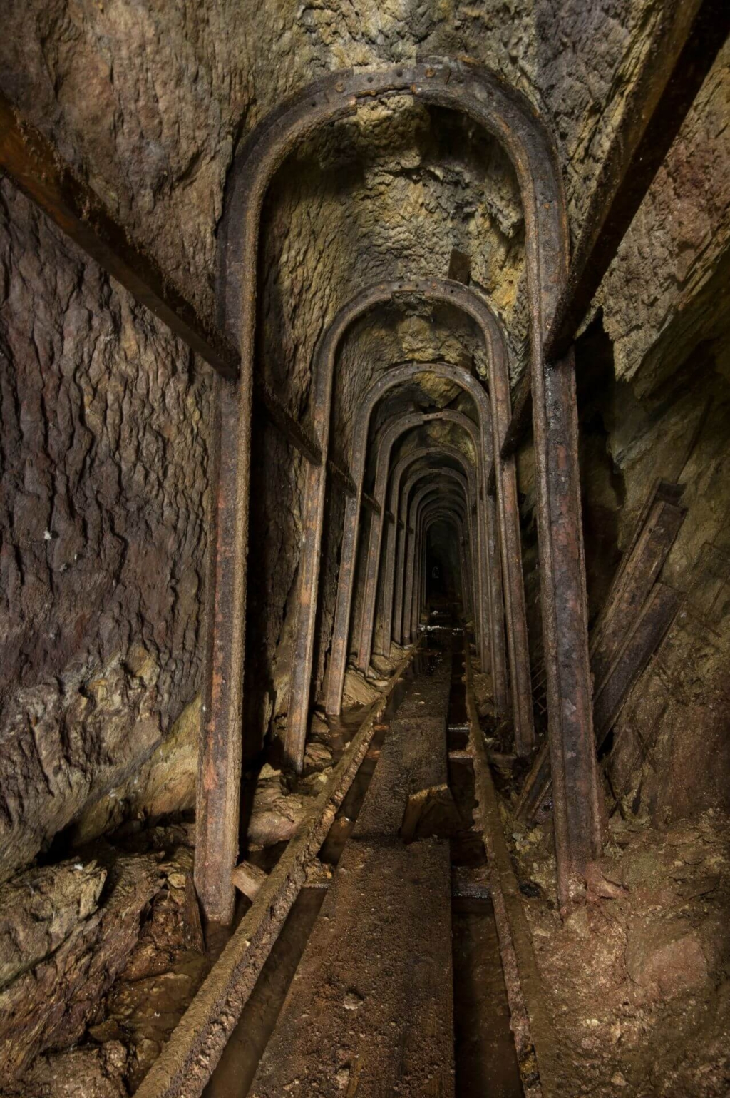 Zeigt Stahlsegmentausbauten und Gleise im Stollen. Zwischen den Schienen liegen noch die alten Bretter, auf denen die Bergmänner liefen.