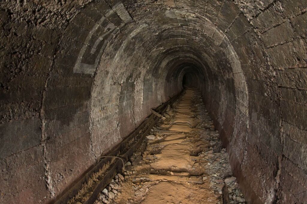Zeigt einen langen, runden Stollen. Die Gleise wurden zurückgebaut, links verläuft die Wasserrinne.