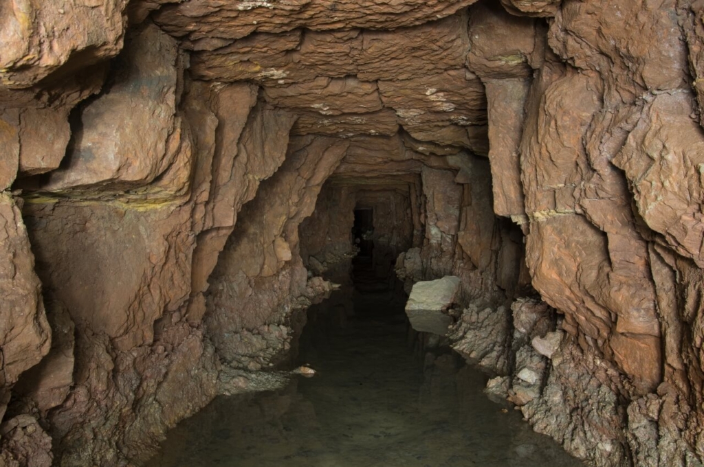 004-tortenstollen Blick in den flachen Stollen zum Abbau, im Stollen steht 20 cm Wasser. Das Gestein ist rot und schroff.