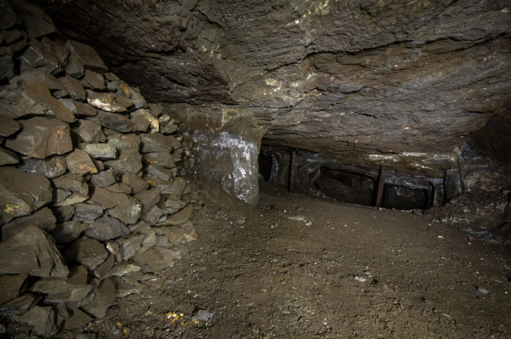 Zeigt einen Kammer-Pfeilerbau mit Versatzmauerung und Holzstempeln im Erzabbau.