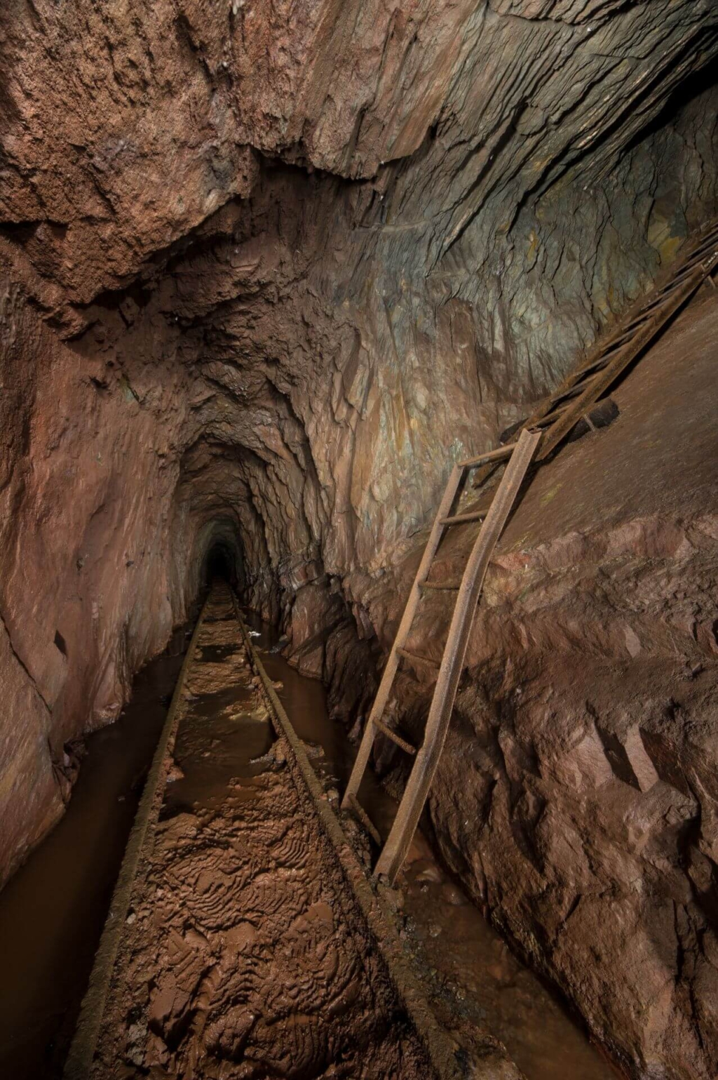 Blick in den Erbstollen mit seinem roten Gestein. In der Mitte liegen Gleise und rechts führt eine Leiterin den Abbau.