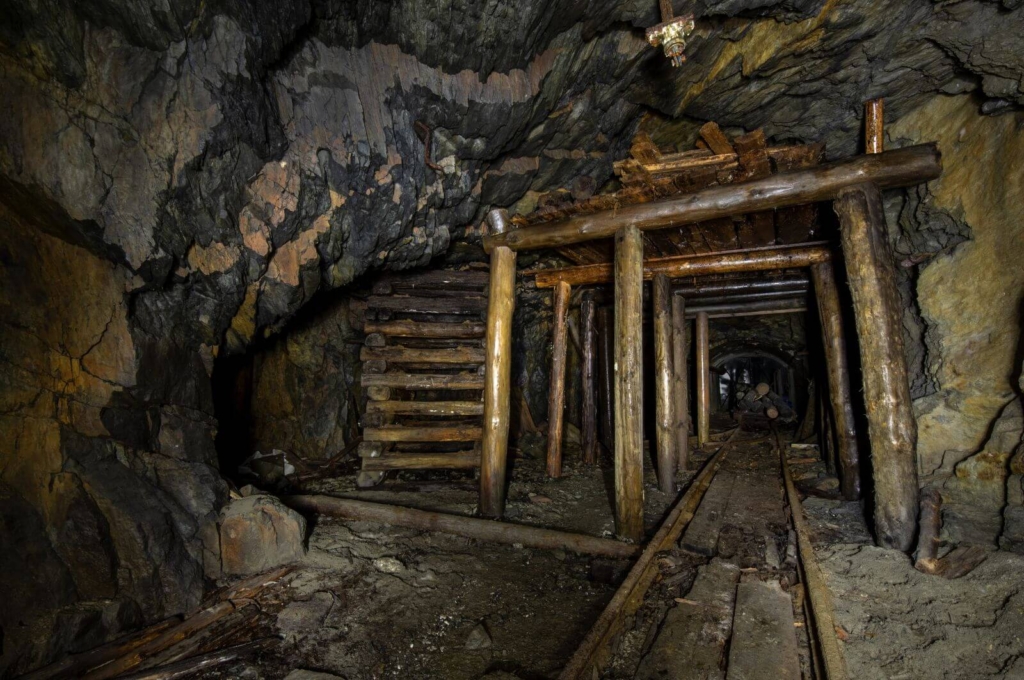 Zeigt einen massiven Streckenausbau mit Türstöcken und Holzkastenpfeilern im Förderstollen.