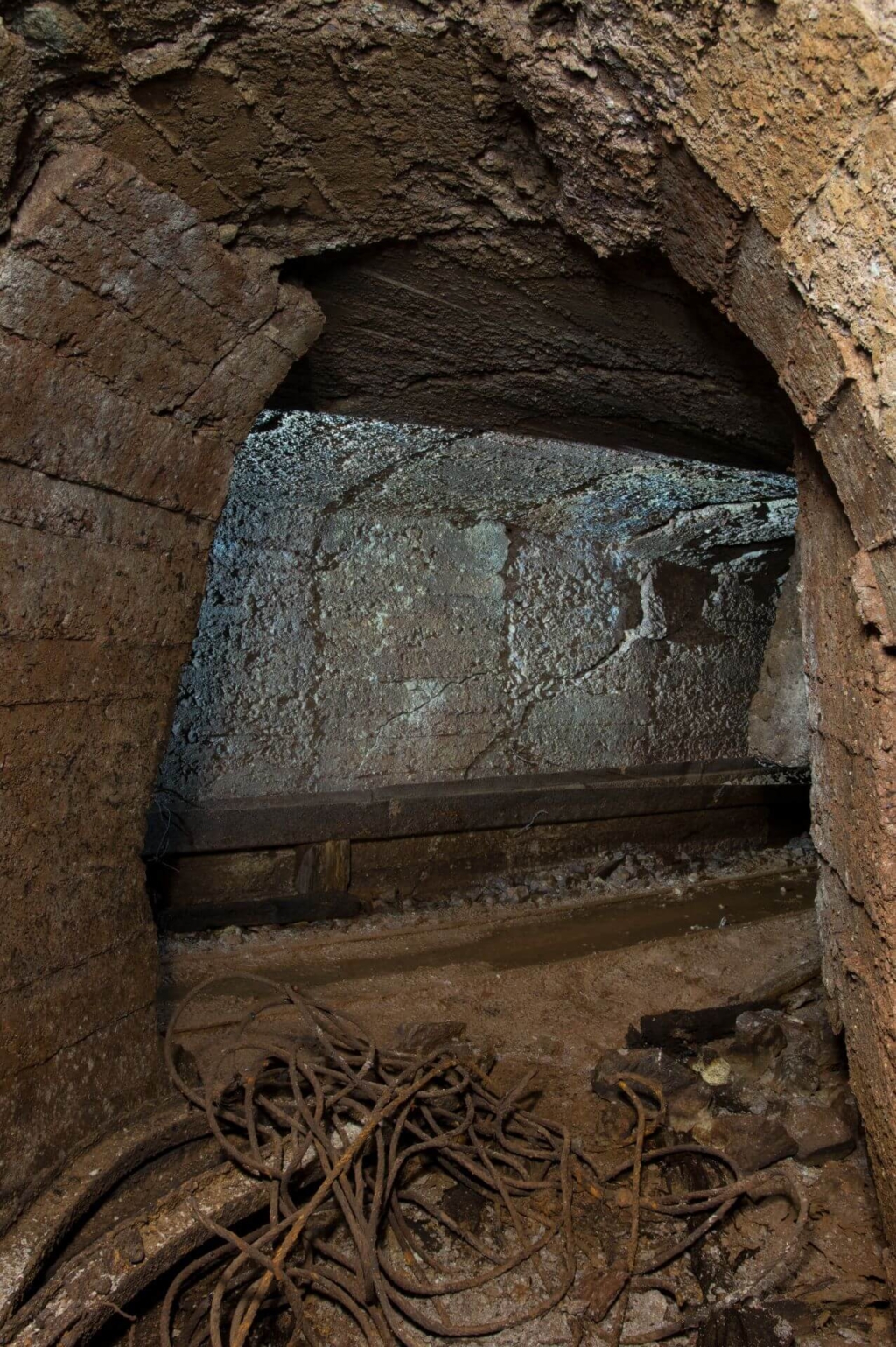 Zeigt den Abzweig vom Hauptstollen auf einen Querschlag. Am Boden liegen rostige Stahlseile.