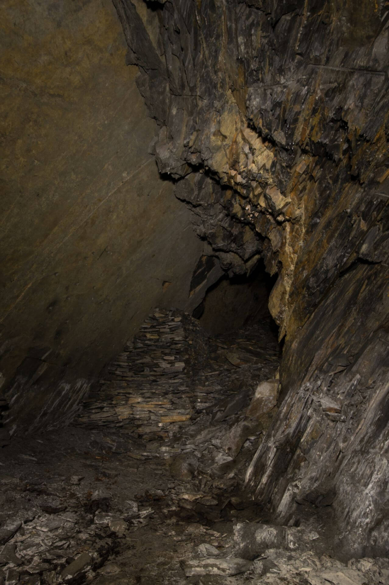 Blick in die Abbaukammer. Rechts schroffes Schiefergestein und links eine glatte Schieferwand. Weiter hinten ist eine Versatzmauer zu sehen.