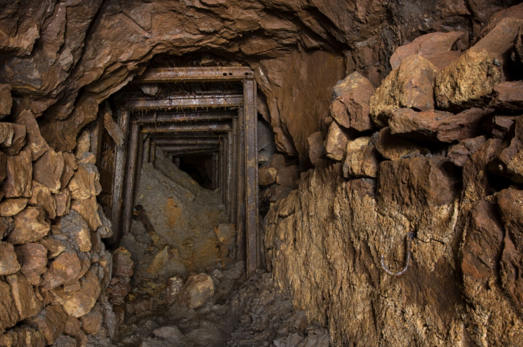 007-tortenstollen Zeigt einen massiven Türstockausbau aus Eisenbahnschienen, welche einen Verbruch abstützen.