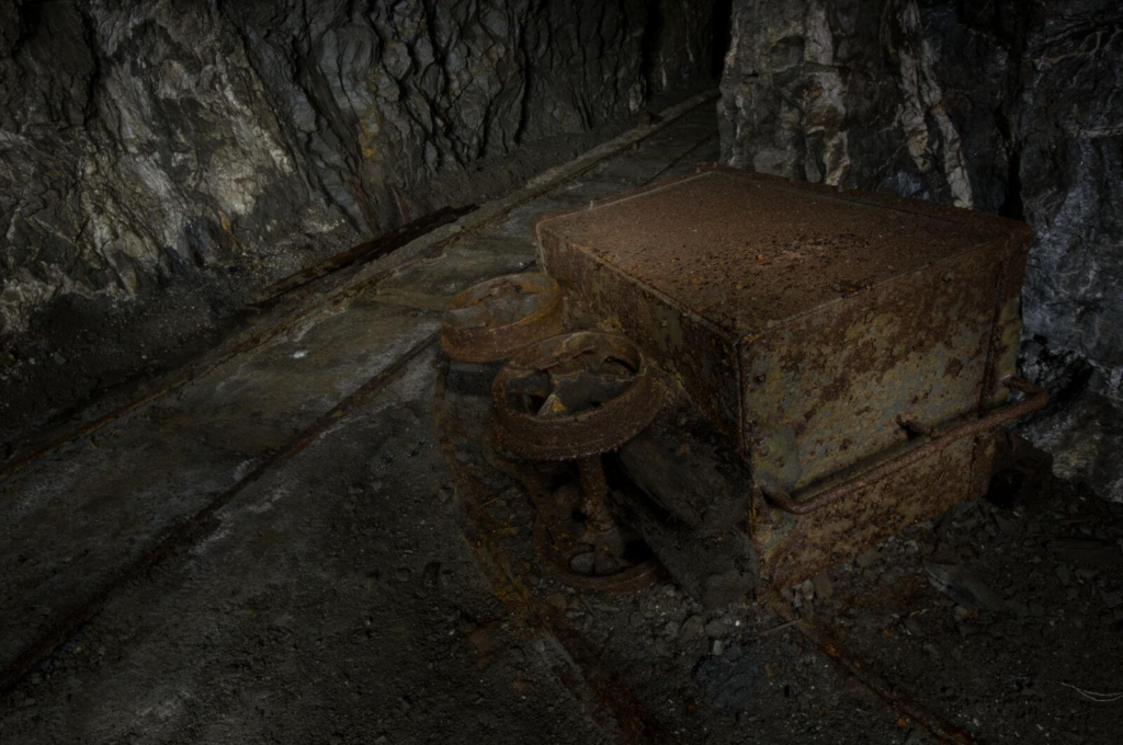 Zeigt einen umgefallenen Förderwagen im Streckenabzweig. Im Hintergrund verlaufen die Gleise der Grubenbahn.