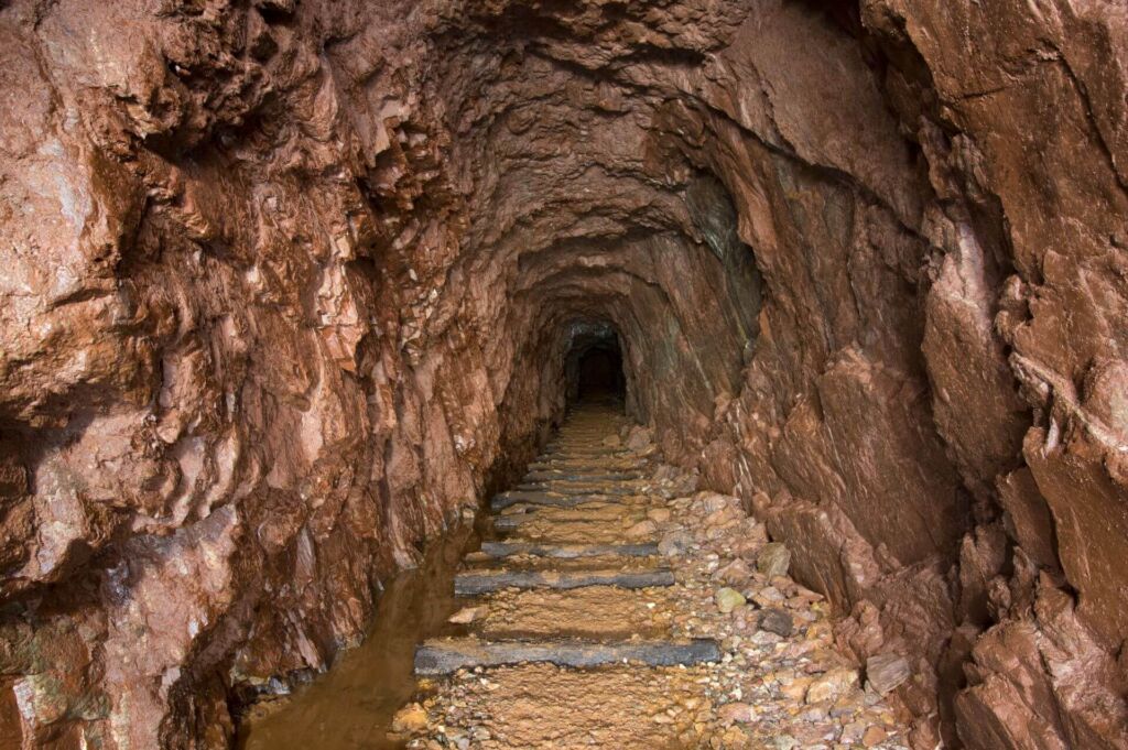 Schroffer Stollen im Roteisengestein. Am Boden liegen noch die Gleisschwellen und links läuft das Wasser Richtung Mundloch.