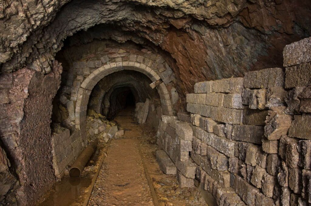 Zeigt einen Streckenabschnitt im Altbergbau. Rechts lagern Fertigbetonsteine zum Stollenausbau.