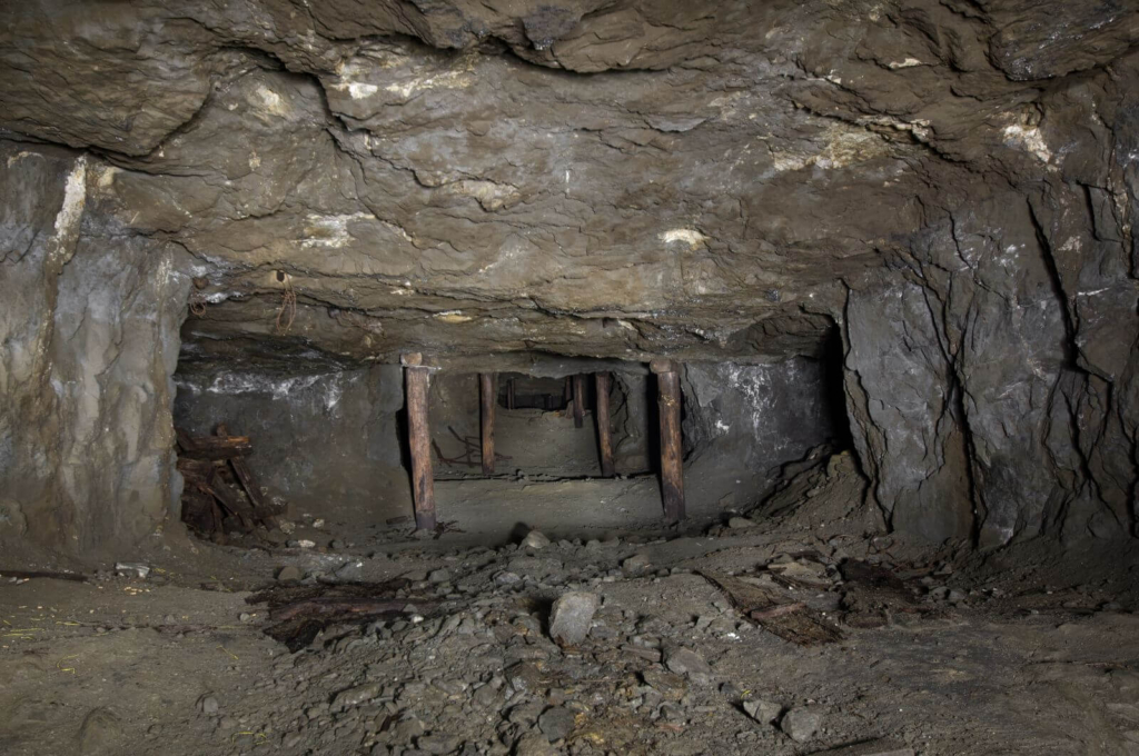 Zeigt eine Schrapperstrecke im Kammer-Pfeilerbau, links und rechts stehen Holzstempel zum Sichern der Firste.