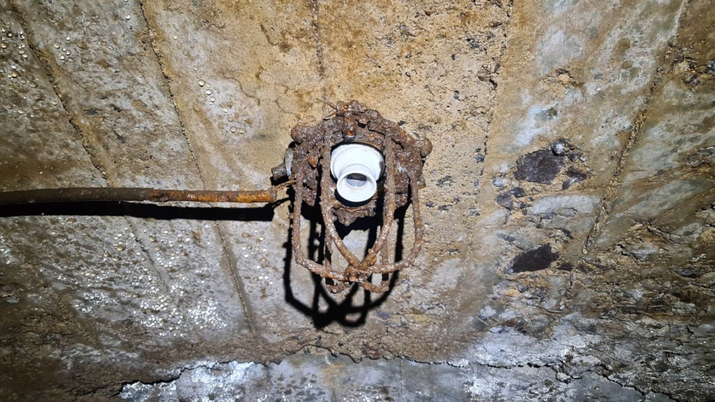 Zeigt die alte verrostete Lampenfassung im Förderstollen. Die innere Porzellanhalterung ist schneeweiß.