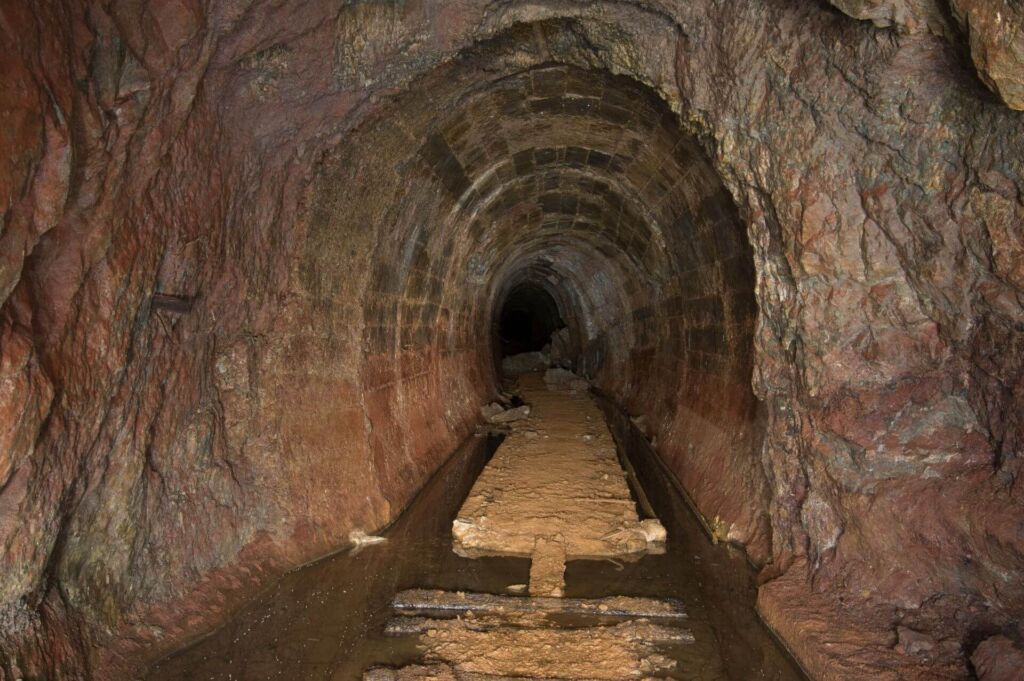 Stollen mit rundem Ausbau aus Betonfertigteilen. Links und rechts vom Gleisbett steht das Wasser