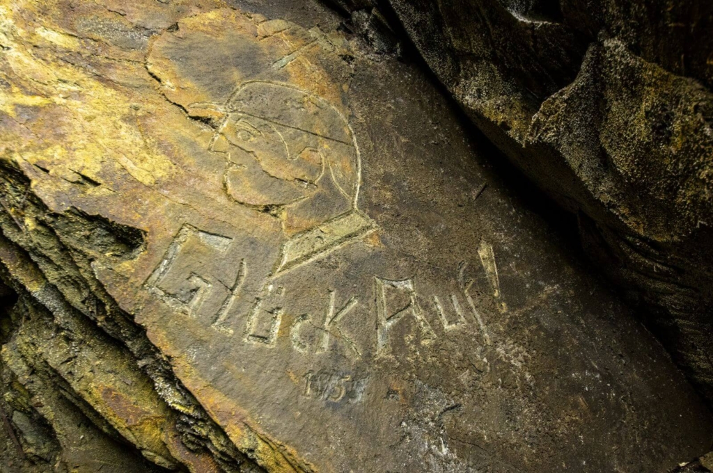 Zeigt einen Bergmann im Profil als Relief in den Fels geschlagen. Mit der Aufschrift "Glück auf 1955"