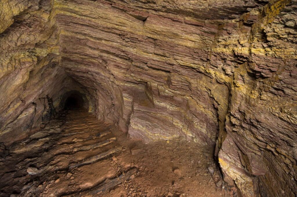 Zeigt einen Stollen mit feiner braunrot gelber Schichtung. Auf der Sohle liegen die Schwellen der Gleise.