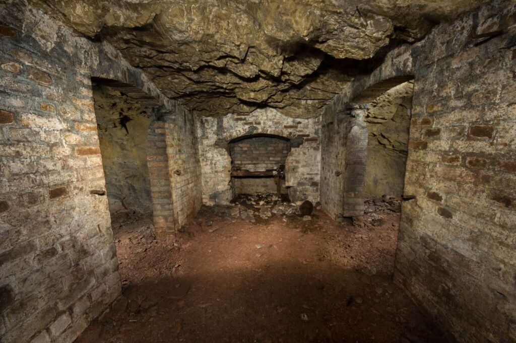 Zeigt einen kleinen Raum mit jeweils einer Tür links und rechts zu weiteren Kammern. Sie dienten der Lagerung von Sprengmitteln.