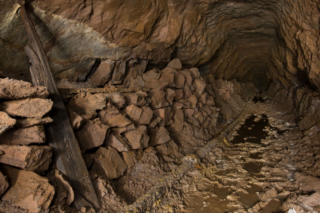 016-tortenstollen Zeigt den Stollen kurz vor dem Verbruch. links ist Gestein gestapelt und eine rostige Druckluftleitung liegt auf dem Boden.