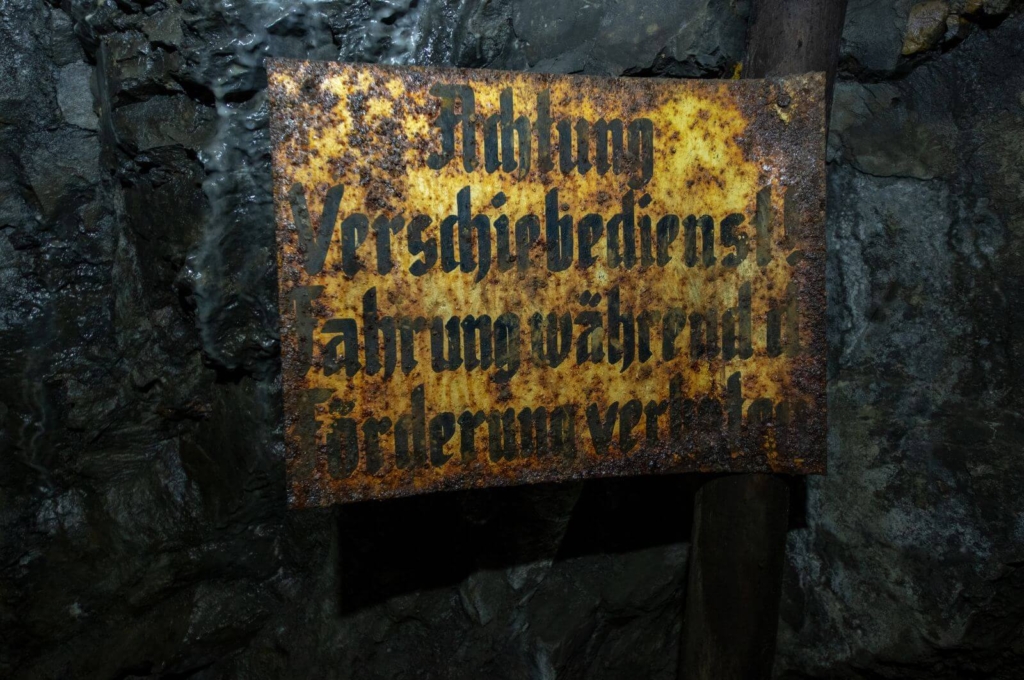 Zeigt ein rostiges Schild mit der Aufschrift "Achtung Verschiebedienst! Fahrung während der Förderung verboten!"