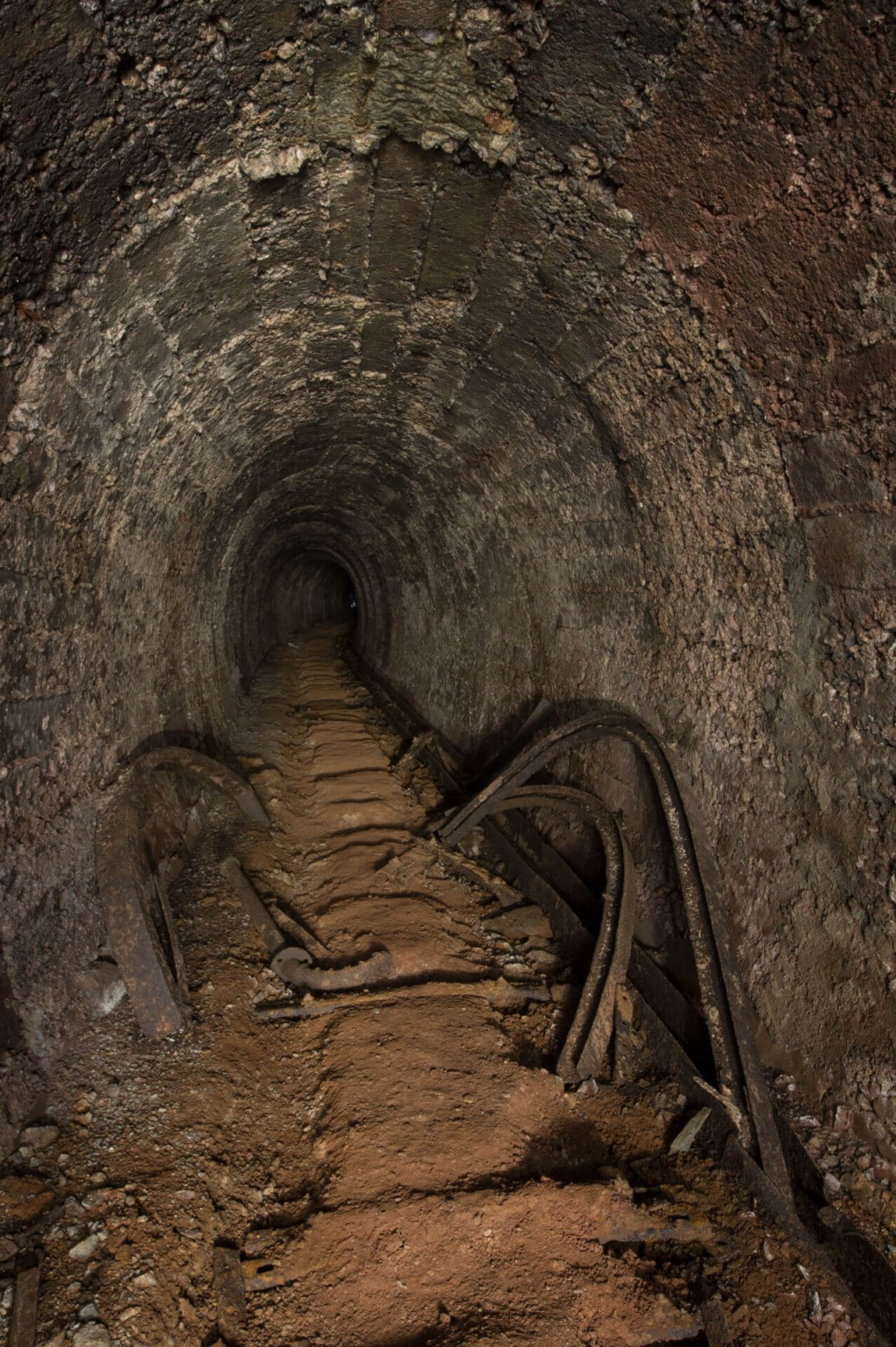 Zeiht einen Altbergbau-Stollen in Betonausbau. Die Gleise fehlen bereits und an den Wänden stehen Stahlteile des Ausbaus.