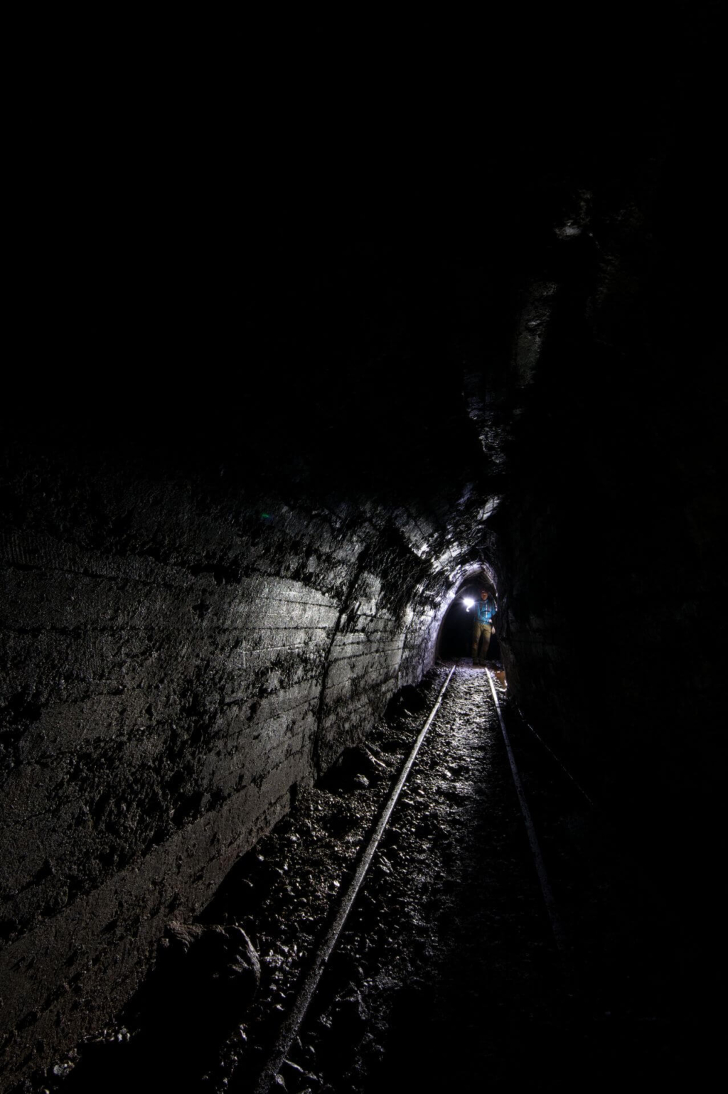 Dunkler Stollen mit Schienen und einer Person am Ende des Stollens.
