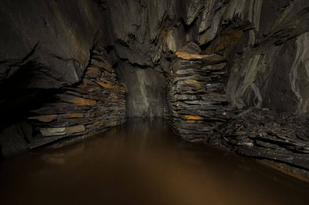 Zeigt eine kleine Abbaukammer mit Trockenmauerungen aus Schieferplatten. Der Raum steht bis zur Hälfte unter Wasser.