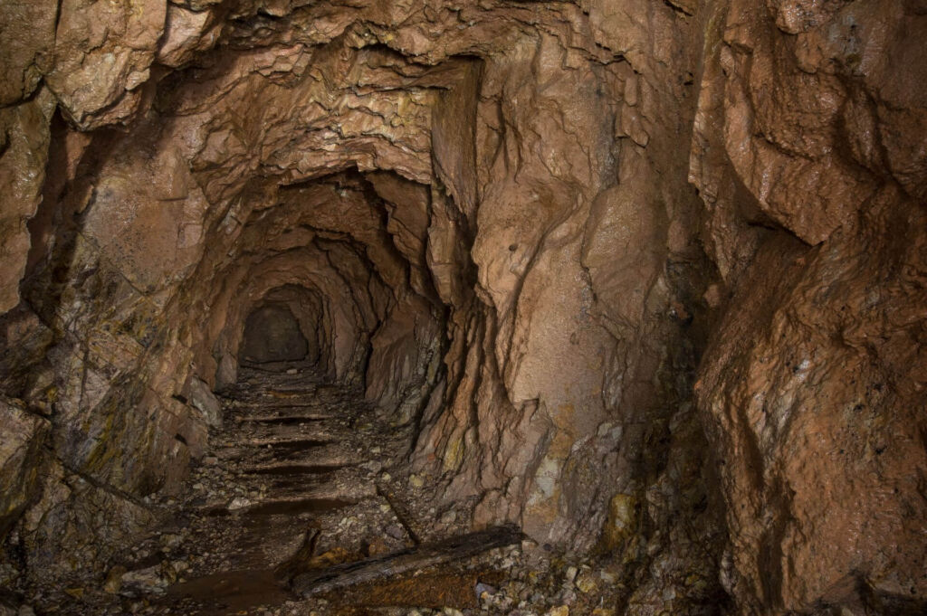 Zeigt eine bergbauliche Strecke in rotem Gestein, auf der Sohle sind die Einkerbungen der Gleisschwellen erkennbar.