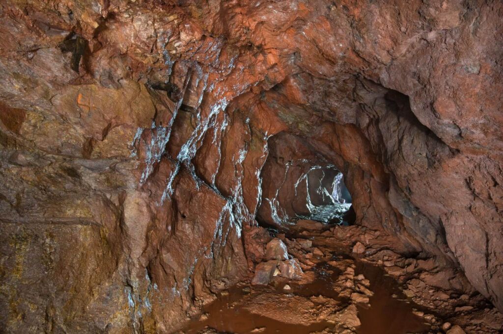 Zeigt einen Stollen im roten Gestein, aus der Ferne strahlt Licht.