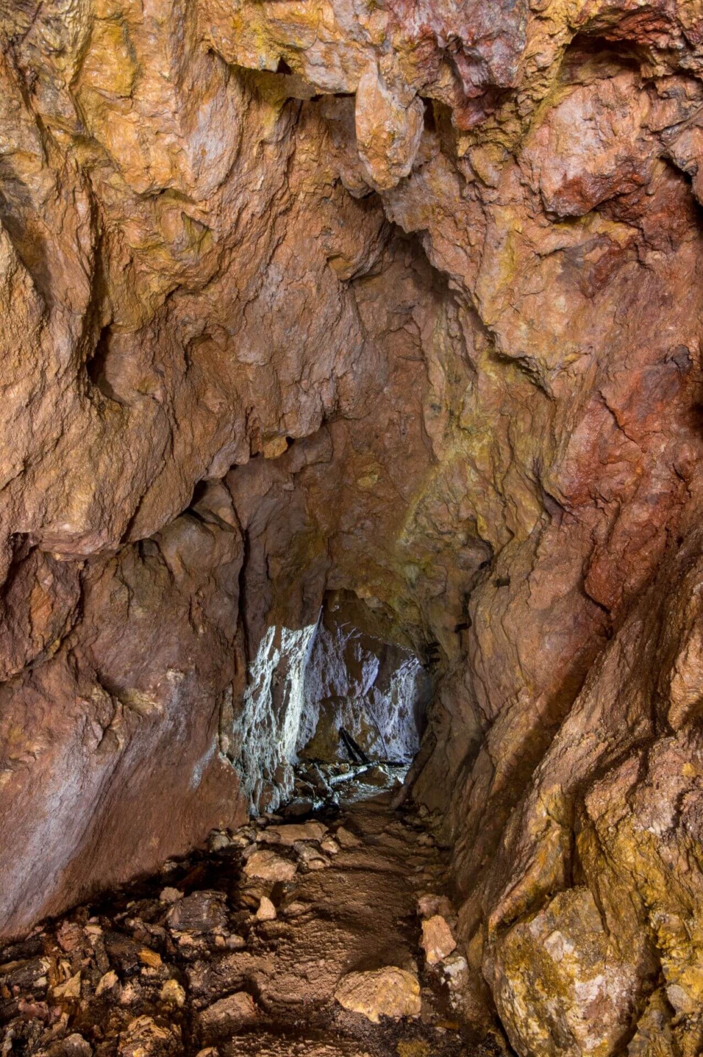 Zeigt einen Stollen im Gegenlicht, die Felswände sind rötlich gefärbt.