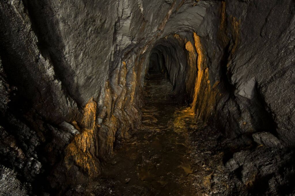 Zeigt einen Schieferstollen mit orangen Versinterungen am linken und rechten Stoß.