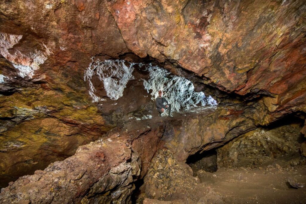 Zeigt eine Person, die im Abbau sitzt, rechts aus dem Stollen scheint Licht auf die Person.