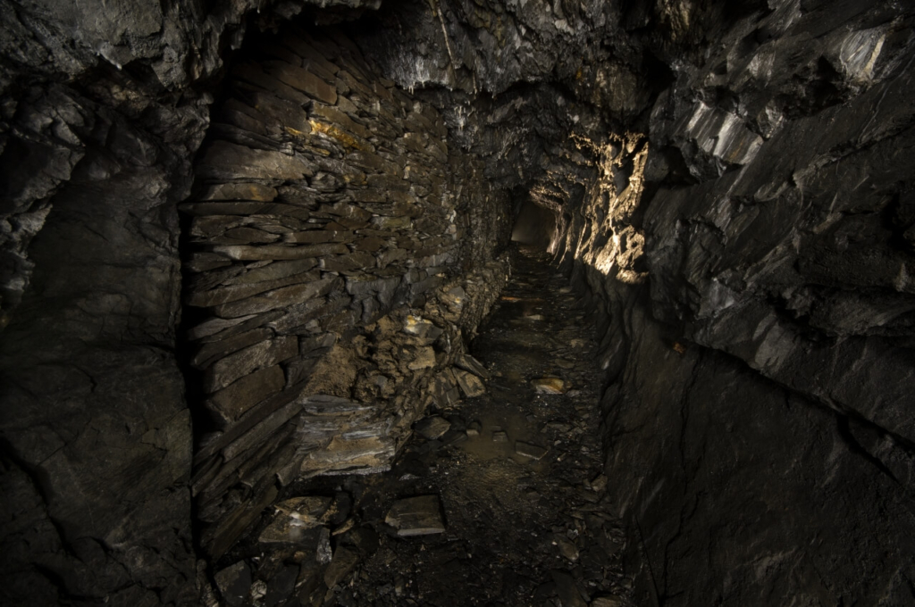 Zeigt einen schroffen dunklen Schieferstollen mit einer großen und langen Versatzmauer auf der linken Seite.