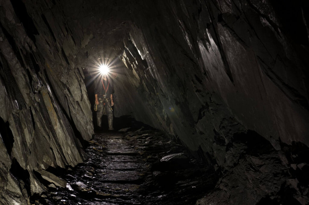 Eine Person steht im Schieferstollen und das Licht seiner Helmlampe erzeugt einen Blendstern in der Kamera.