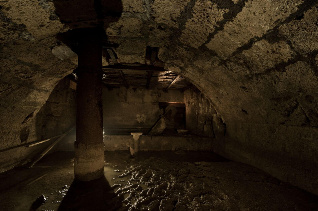 Zeigt die Gewölbemauerung aus Sandstein in der unterirdischen Flussumleitung. Aus der Decke kommt ein dickes rostiges Rohr.