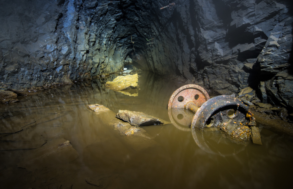 001_achse Zeigt einen Stollen, in dem 20 cm tiefes Wasser steht. Im Wasser liegt die Achse einer Lore.