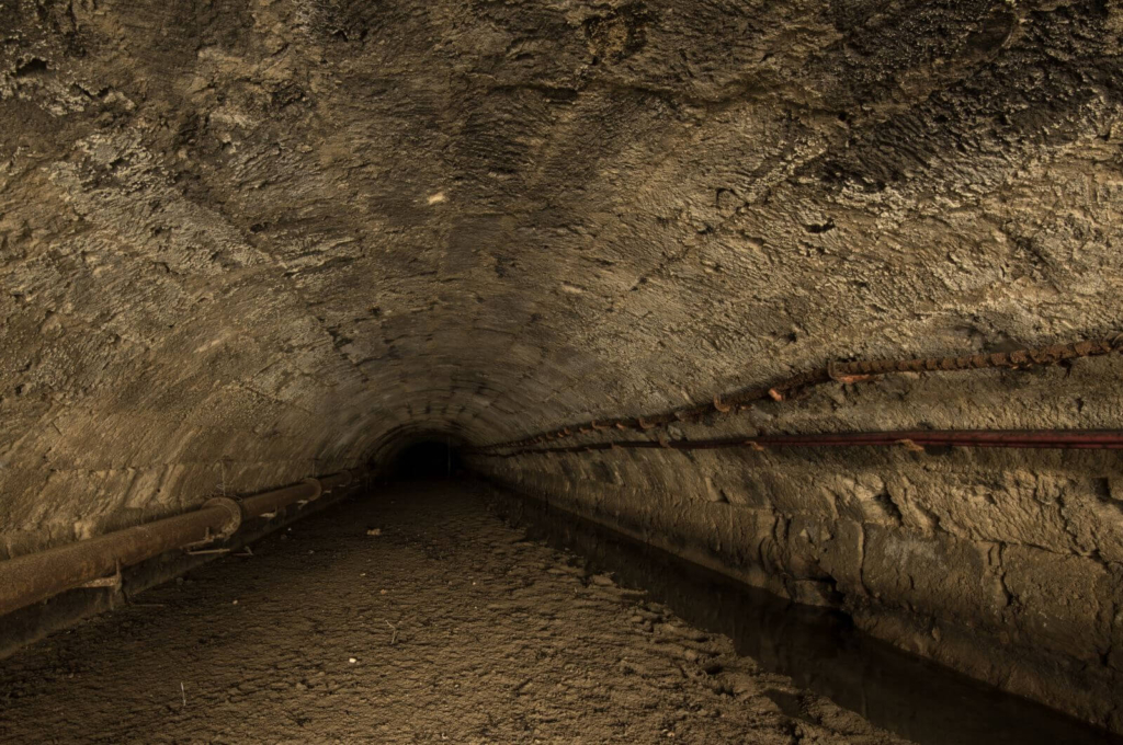 Das ehemalige unterirdische Flussbett der Flussumleitung in Gewölbemauerung. Das Gewölbe besteht aus Sandstein und der Boden ist schlammig.