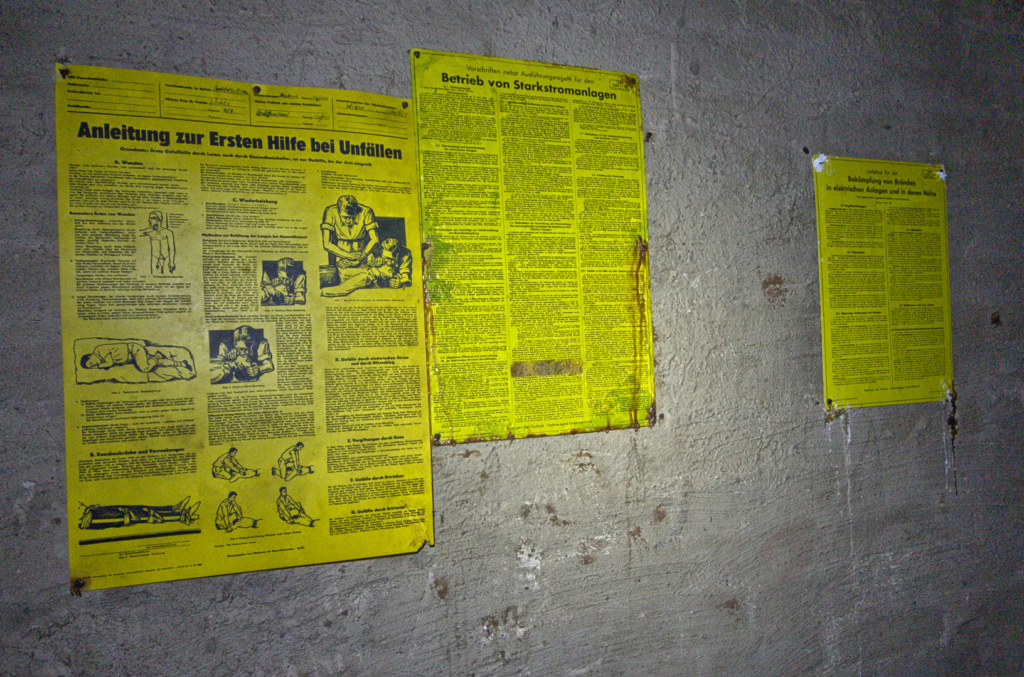 005_erste_hilfe Zeigt gelbe Schilder an der Wand, auf denen Erste Hilfeanleitungen stehen.