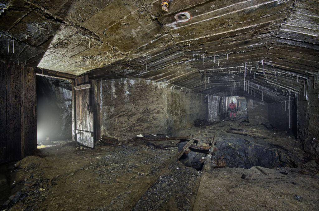 007_verbruch Zeigt einen in Beton ausgebauten Stollen. Am Boden klafft ein riesiges Loch über dem Gleise führen.