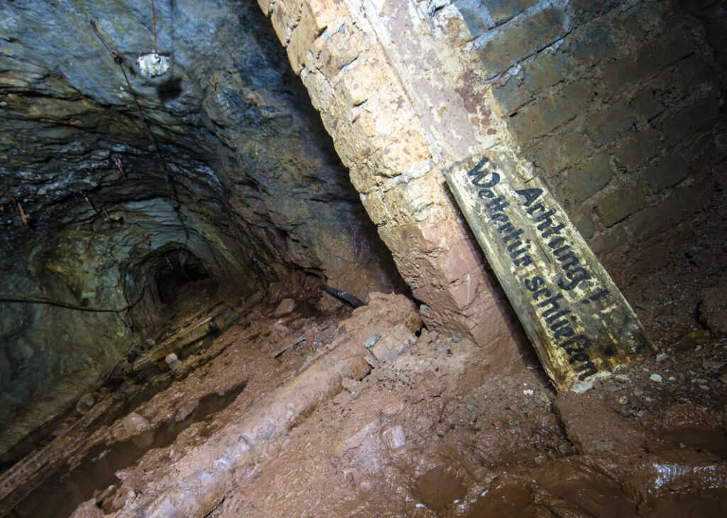007_wettertuer_schließen Zeigt einen Stollen und ein Schild, das an der Ziegelmauer lehnt.