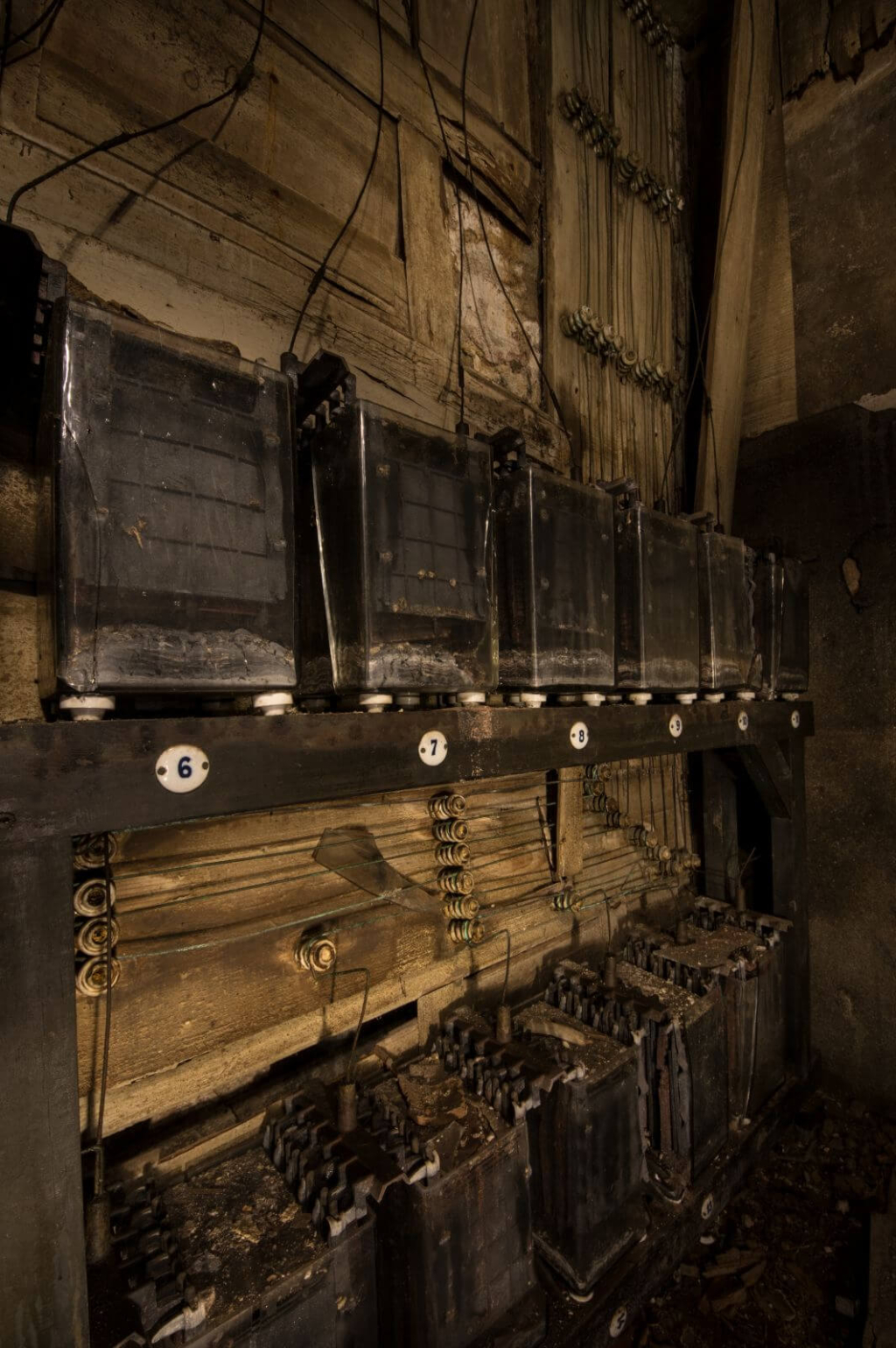 Nahaufnahme der Bleiakkus und ihrer akkuraten Verdrahtung. Auf das Regal sind kleine ovale Emailleschilder mit der Akkunummer genagelt.