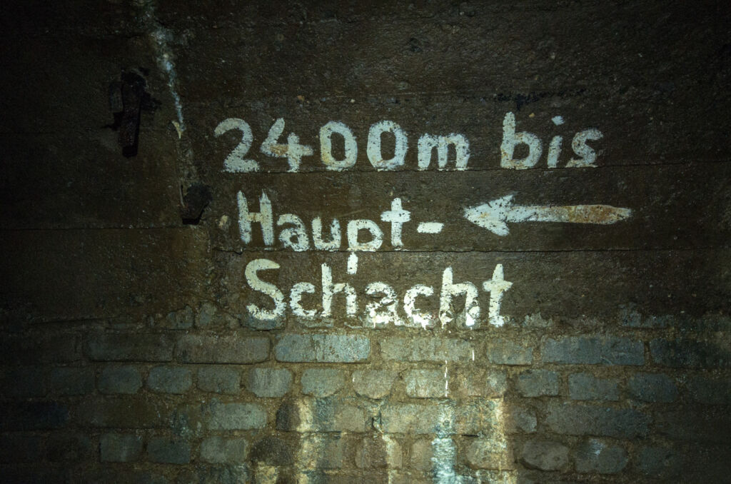 009_hauptschacht Zeigt eine Wand mit weißer Aufschrift "2400 Meter bis zum Hauptschacht".