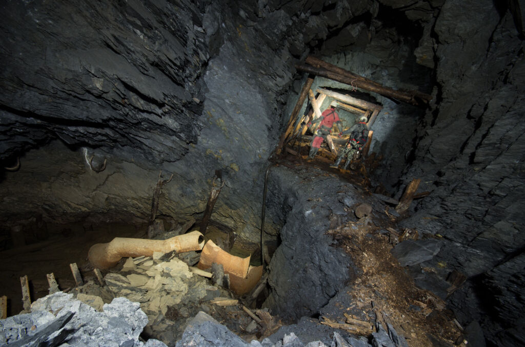 012_hand_in_hand Zeigt zwei Personen in dunklen Stollen die Hand in Hand dastehen. Links im Bild ein Gesenk mit Wasser