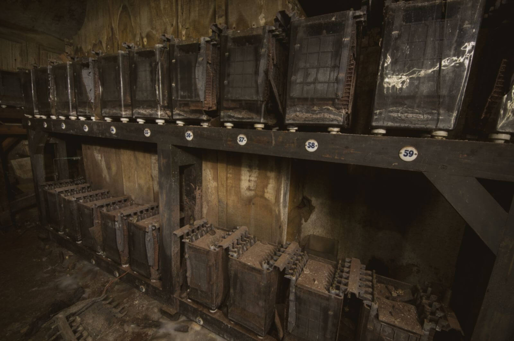 Nahaufnahme der Bleiakkus und ihrer akkuraten Verdrahtung. Auf das Regal sind kleine ovale Emailleschilder mit der Akkunummer genagelt.