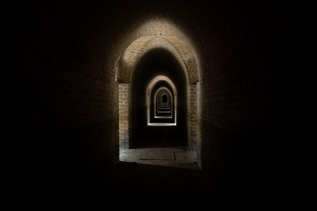 Langer Flur im Tonnengewölbeausbau, aus den anliegenden Türen strahlt Licht.