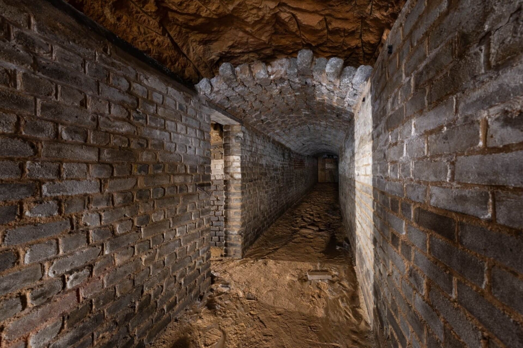 Luftschutzstollen mit flachem Ziegelgewölbeausbau, links eine Tür zum Schutzraum.