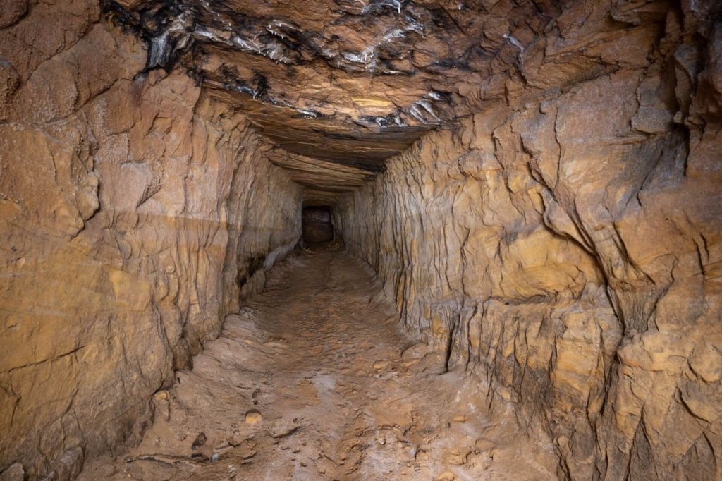 Flacher unausgebauter Stollen im gelben Sandstein und sandigen Boden.