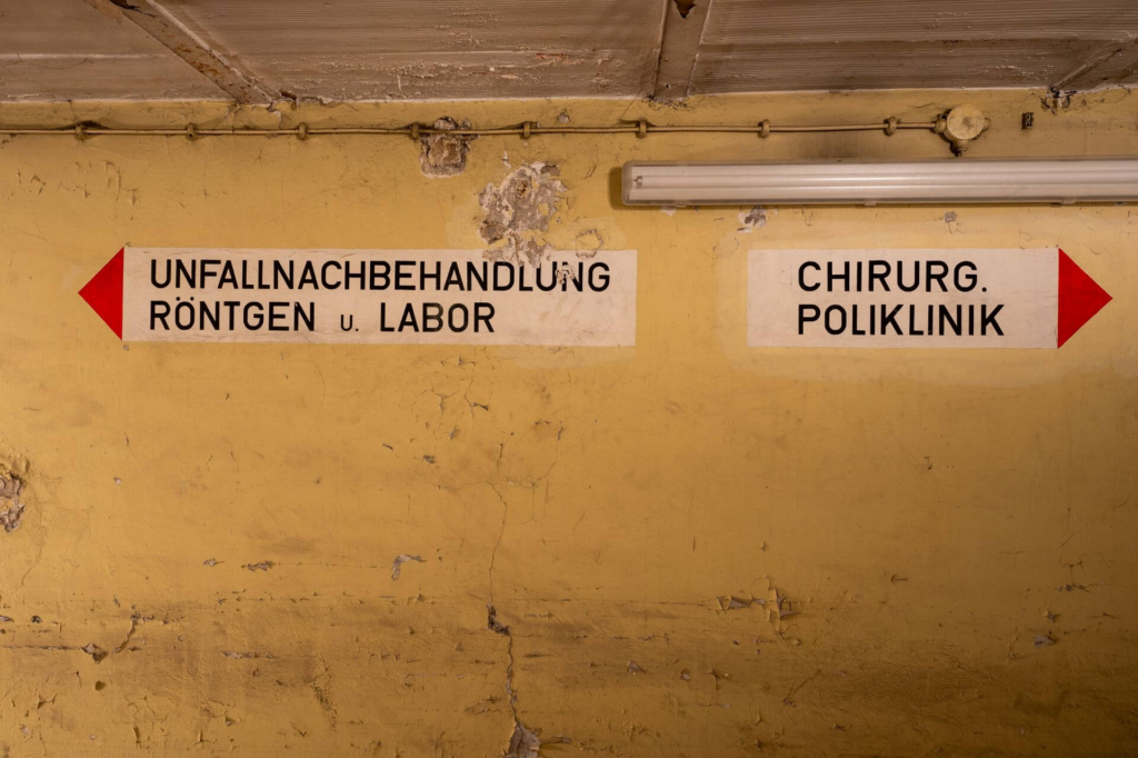 Beschriftung im Zugangsflur als Wegweiser. Links "Unfallnachbehandlung Röntgen und Labor". Rechts "Chirurg. Poliklinik"
