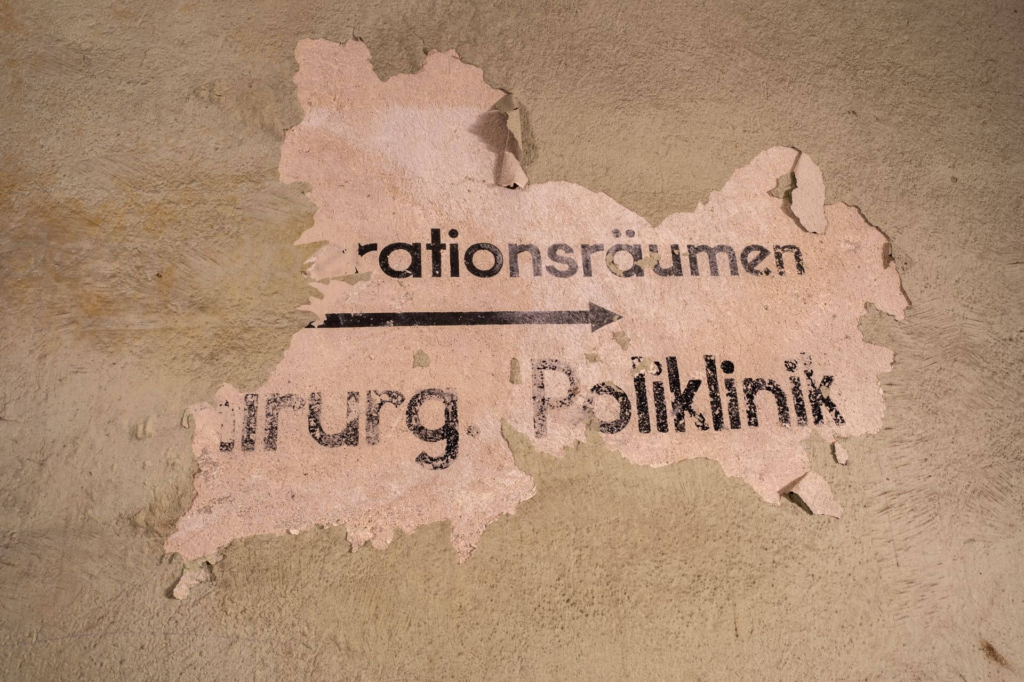 Die Farbe der Wand blättert ab und darunter findet sich eine alte Beschriftung "Chirurgische Poliklinik"