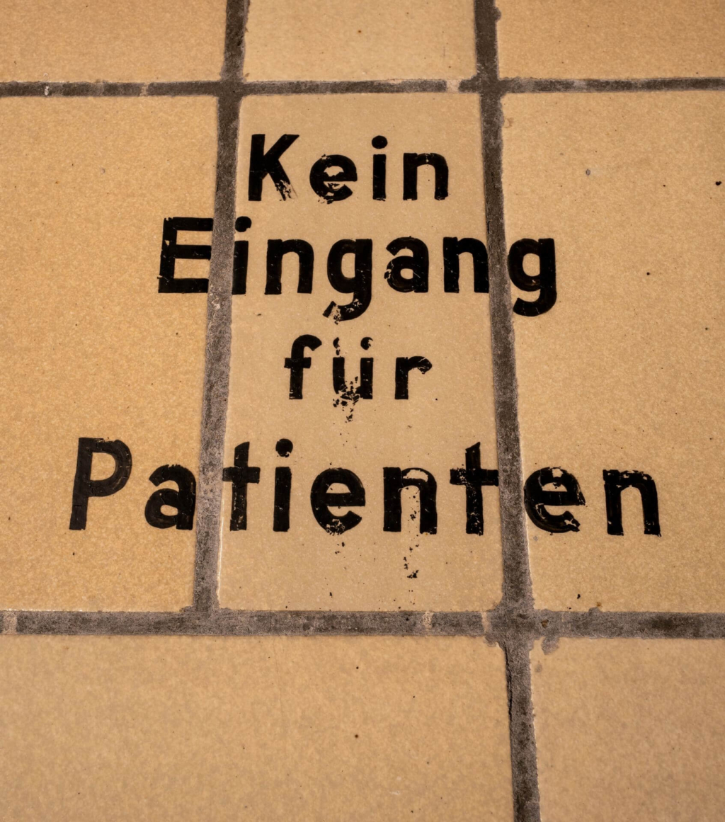 Schwarze Beschriftung auf der Fliesenwand in der Gasschleuse "Kein Eingang für Patienten"