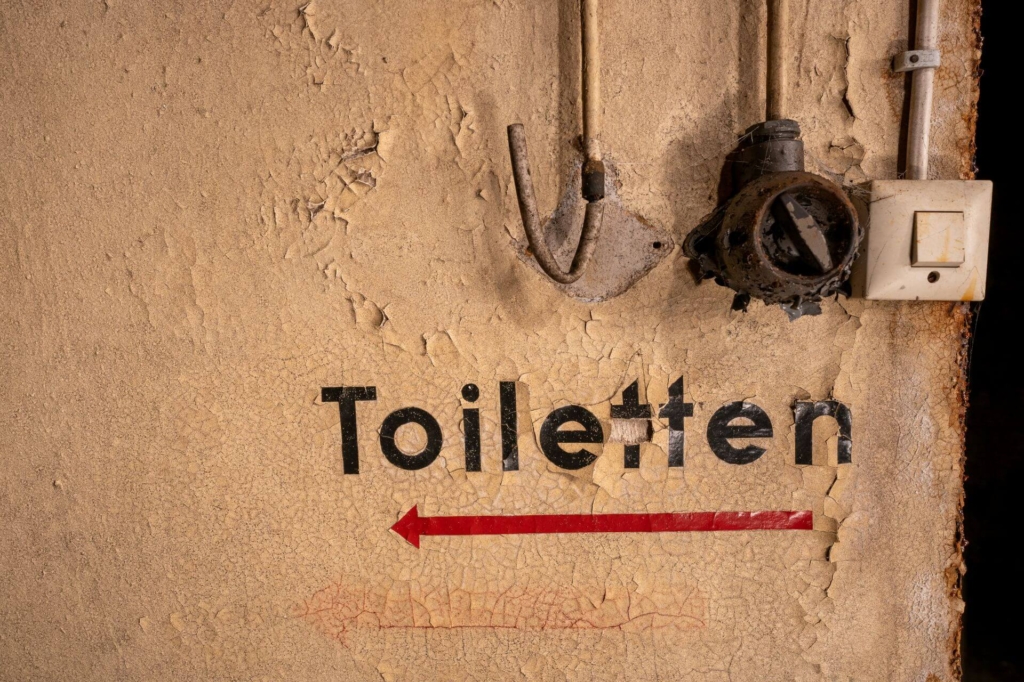 Beschriftung an der Wand "Toiletten" mit rotem Pfeil darunter.