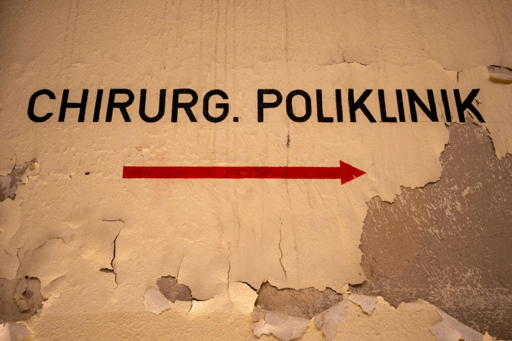Beschriftung an der Wand "Chirurgische Poliklinik", die Farbe blättert ab.